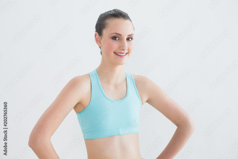 Smiling toned woman with hands on hips against wall Smiling toned woman with hands on hips against wall