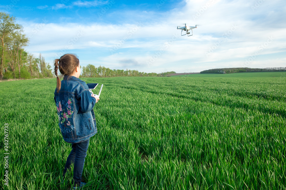 Little girl is operating the drone by remote control in the field