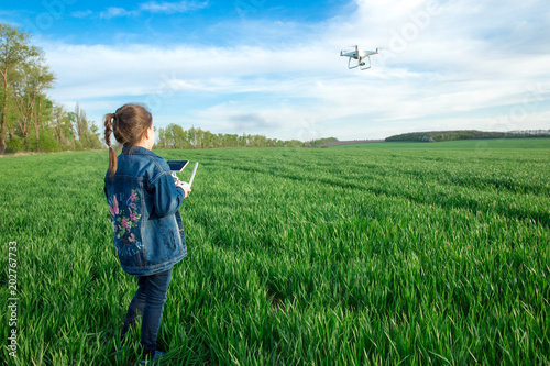 Little girl is operating the drone by remote control in the field