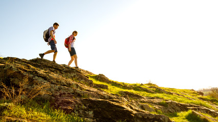 Young Happy Couple Hiking with Backpacks on the Beautiful Rocky Trail at Sunny Evening. Family Travel and Adventure.