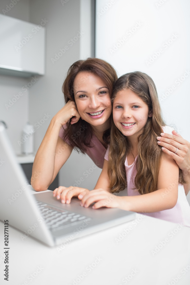 Smiling mother with daughter using laptop in kitchen Smiling mother with daughter using laptop in kitchen