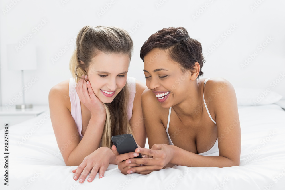 Smiling female friends reading text message in bed Smiling female friends reading text message in bed