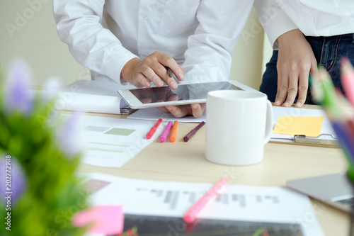 Young business colleagues using a tablet and talking together while standing at a table in a modern office