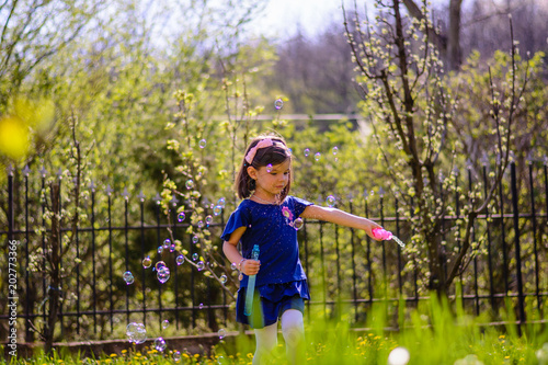 Portrait of a beautiful black hair little girl while playing outside in nature on green grass with bubbles enjoying in carefree childhood