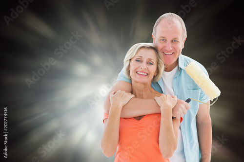 Happy older couple holding paint roller against black abstract light spot design
