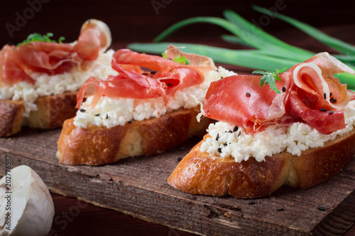 Baguette with cottage cheese, arugula and ham, sandwich on a board, selective focus. Wooden rustic background. Top view