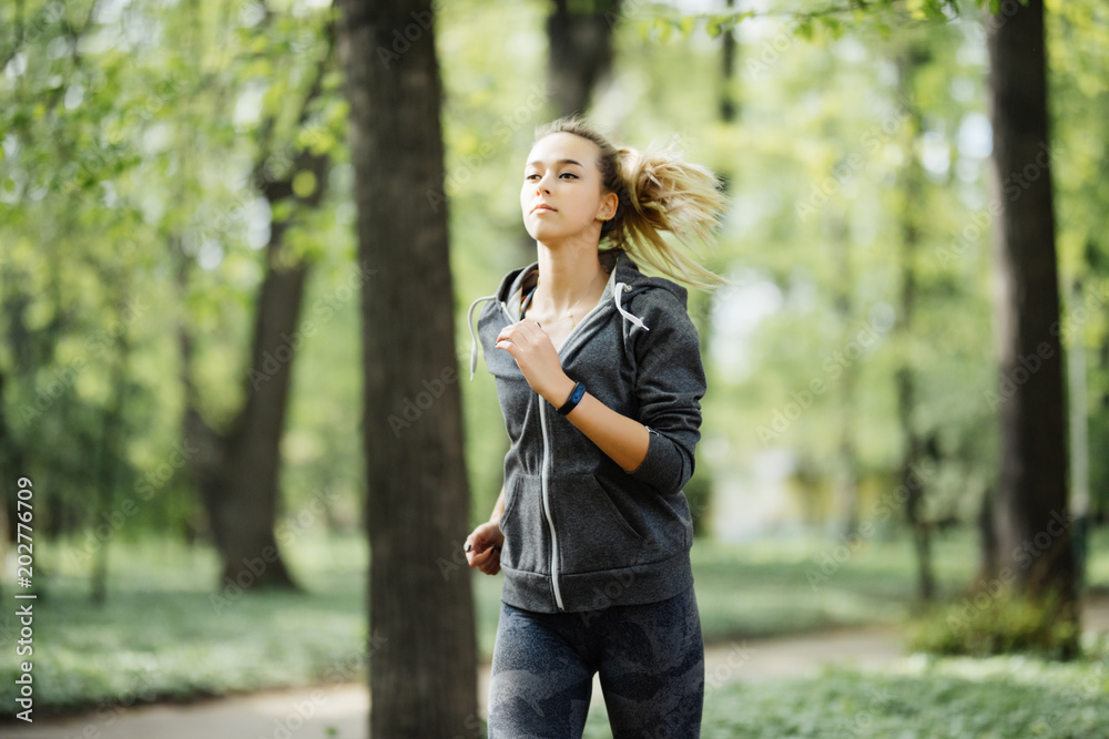 Young smiling sporty woman running in park in the morning. Fitness girl jogging in park Young smiling sporty woman running in park in the morning. Fitness girl jogging in park