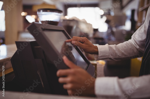 Midsection of waiter touching computer monitor at counter