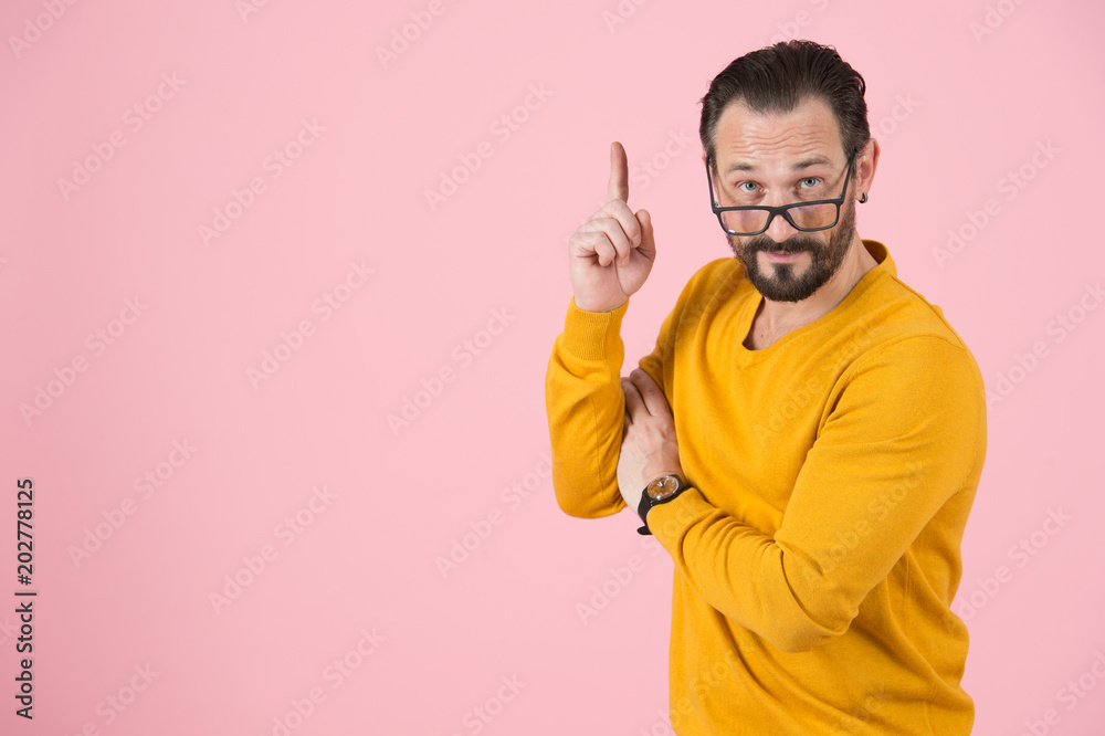 Clever man in glasses pointing up by finger. Bearded man notes by hand up. Wise man asks attention to above. Professor makes conclusion on pink background