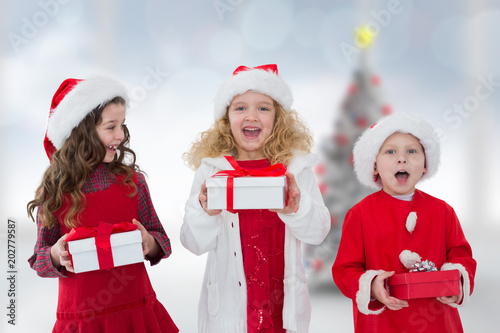 Cute children with gifts against blurry christmas tree in room