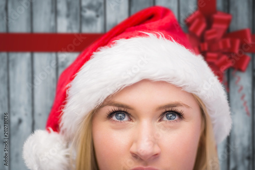 Festive blonde looking up in santa hat against festive bow over wood