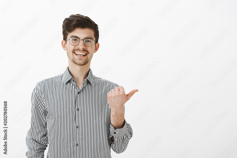 Have you heard what guy said. Portrait of carefree friendly male coworker with moustache and beard, pointing right with thumb and smiling broadly, indicating at person and gossiping about him Have you heard what guy said. Portrait of carefree friendly male coworker with moustache and beard, pointing right with thumb and smiling broadly, indicating at person and gossiping about him