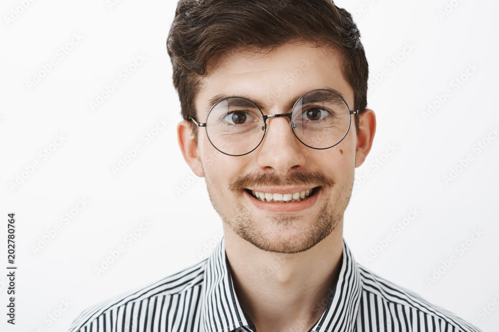 Close-up shot of confident carefree european man with beard and moustache, wearing trendy glasses, smiling broadly and looking with positive expression at camera, liking talking with friend