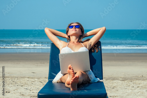 beautiful and sexy young woman lies and rests on a deckchair with a laptop of the sea. woman freelancer with laptop in the resort