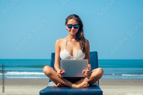 beautiful and sexy young woman sitting in lotus pose and medetiruet on a lounger with a laptop by the sea. woman freelancer doing yoga with a laptop in the resort