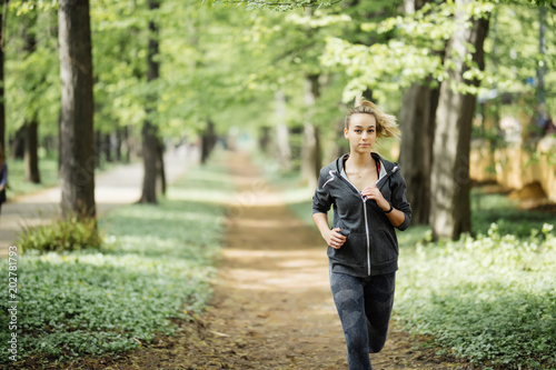 Young smiling sporty woman running in park in the morning. Fitness girl jogging in park