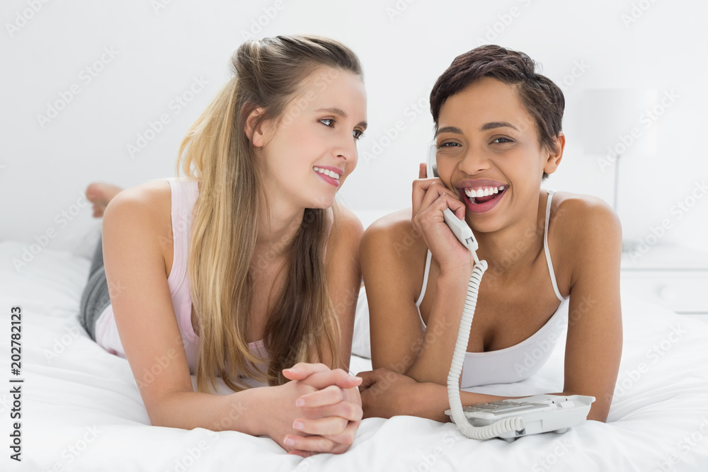 Cheerful female friends using phone while lying in bed Cheerful female friends using phone while lying in bed