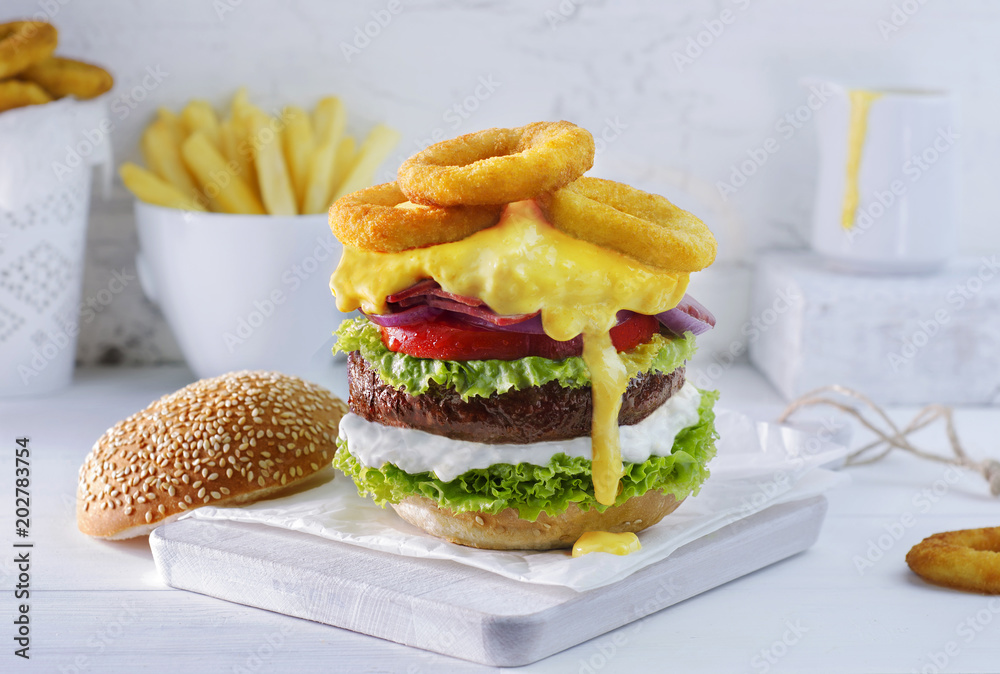 Φωτογραφία Delicious grilled beef burger with layers of lettuce, mayonnaise, tomato,onion, bacon, melted cheddar cheese and fried onion rings