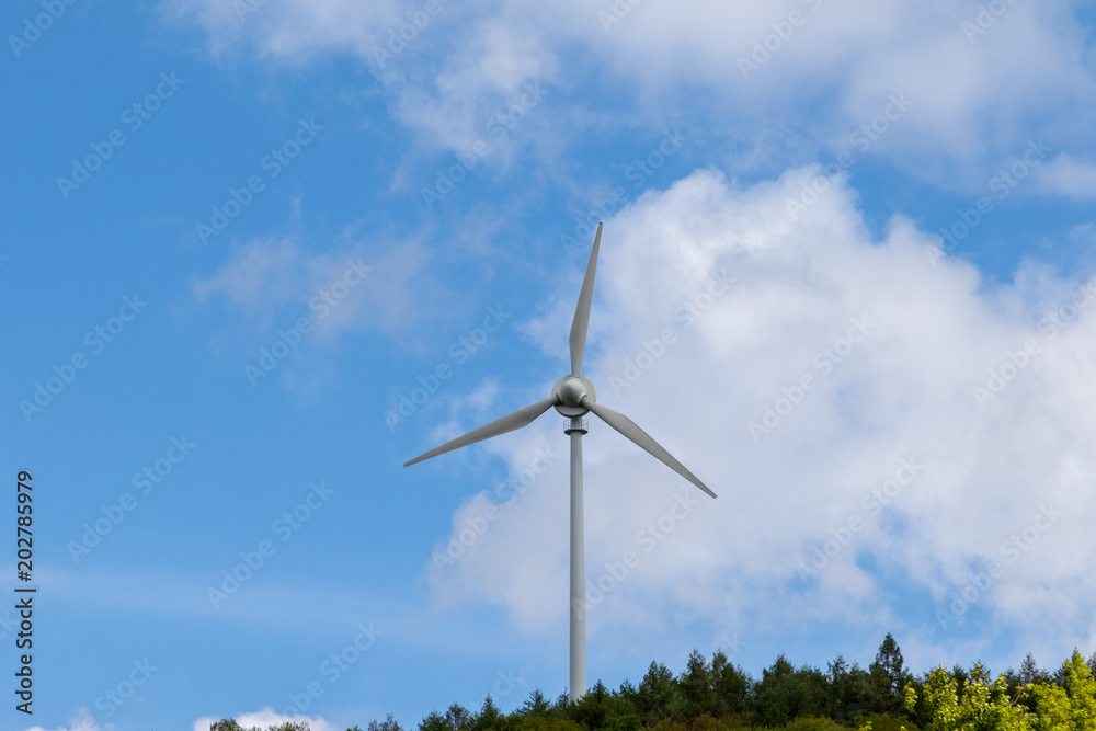 Einzelne Windkraftanlage in einem Waldgebiet vor blauem Himmel Einzelne Windkraftanlage in einem Waldgebiet vor blauem Himmel