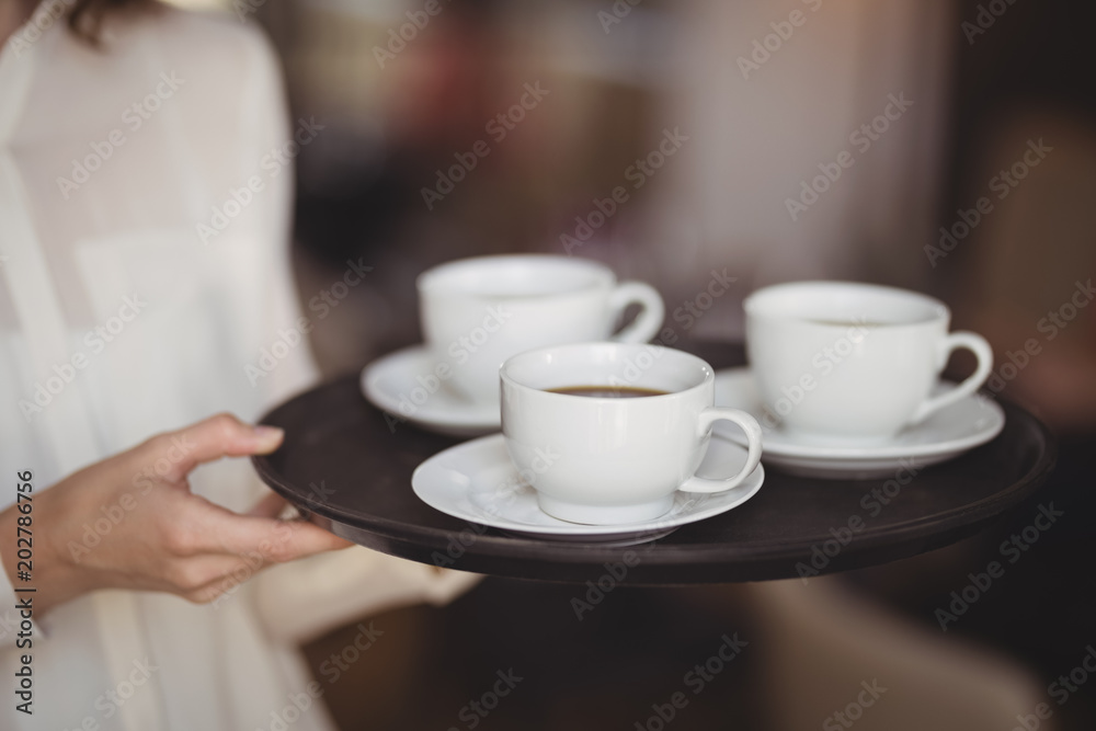 Mid section of waitress holding coffee in tray Mid section of waitress holding coffee in tray
