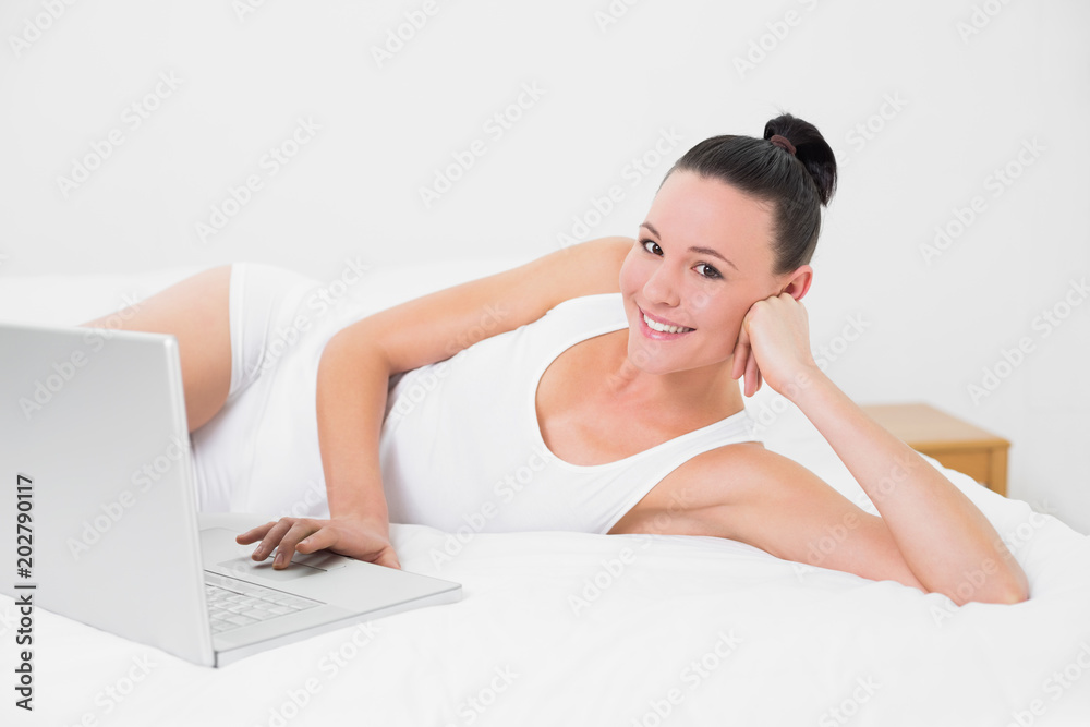 Obraz premium Casual smiling woman using laptop in bed