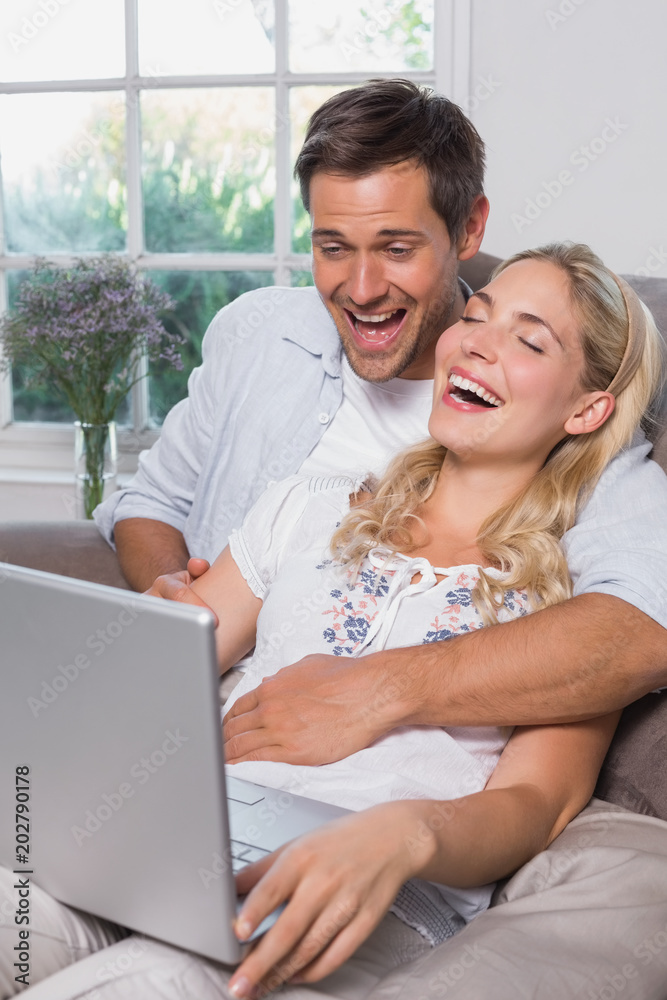 Cheerful casual couple using laptop in living room Cheerful casual couple using laptop in living room