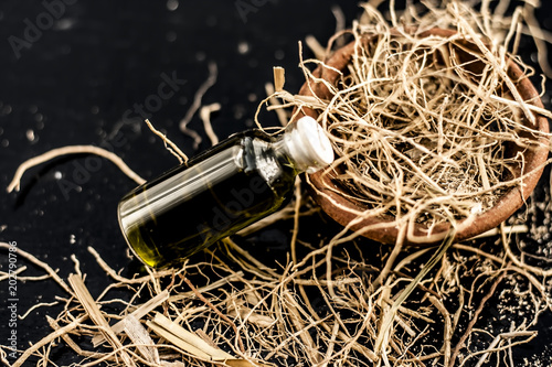 Floral and ayurvedic essence of herb Vetiver grass or Khus in a transparent bottle used in many beverages of Indian and Asia with dried vetiver grass in a clay bowl on black surface.; photo