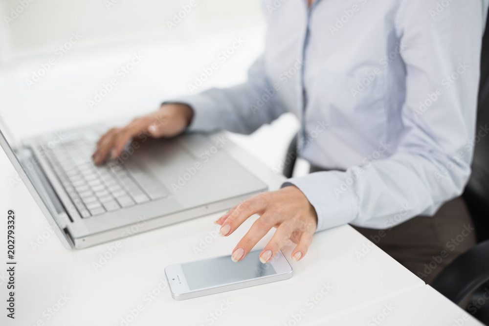 Side view mid section of a businesswoman using laptop and cellphone Side view mid section of a businesswoman using laptop and cellphone