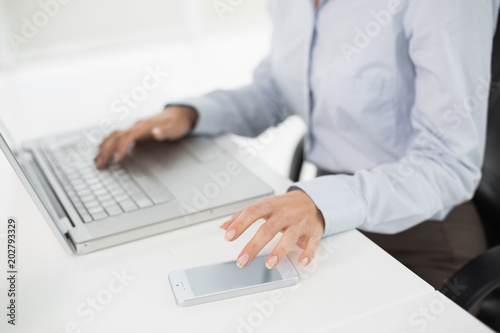 Side view mid section of a businesswoman using laptop and cellphone
