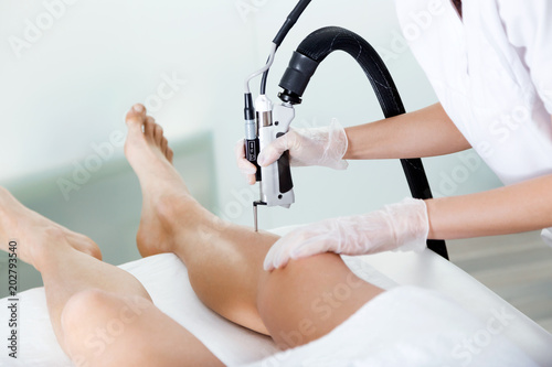 The beautician's hands removing legs hair with a laser to her client in the beauty salon.