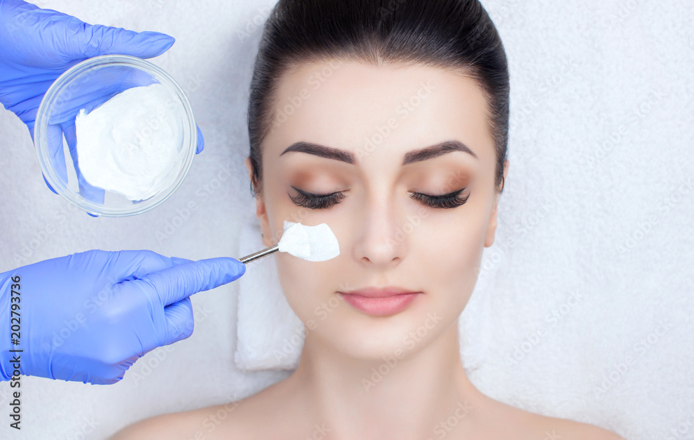 The cosmetologist for the procedure of cleansing and moisturizing the skin, applying a mask with stick to the face of a woman in beauty salon. Cosmetology and professional skin care. The cosmetologist for the procedure of cleansing and moisturizing the skin, applying a mask with stick to the face of a woman in beauty salon. Cosmetology and professional skin care.