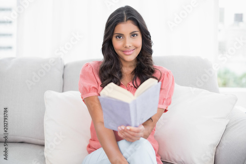 Smiling cute brunette sitting on couch reading a book