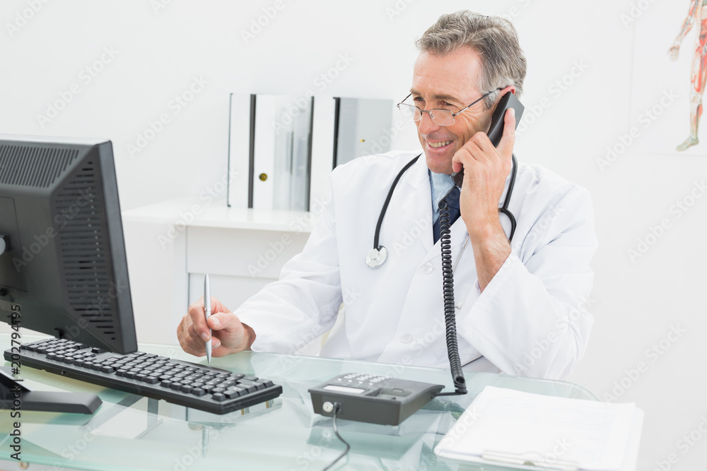 Doctor using computer and telephone at office Doctor using computer and telephone at office