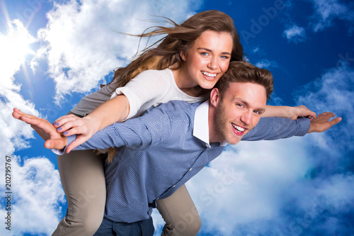 Smiling young man carrying woman against bright blue sky with clouds