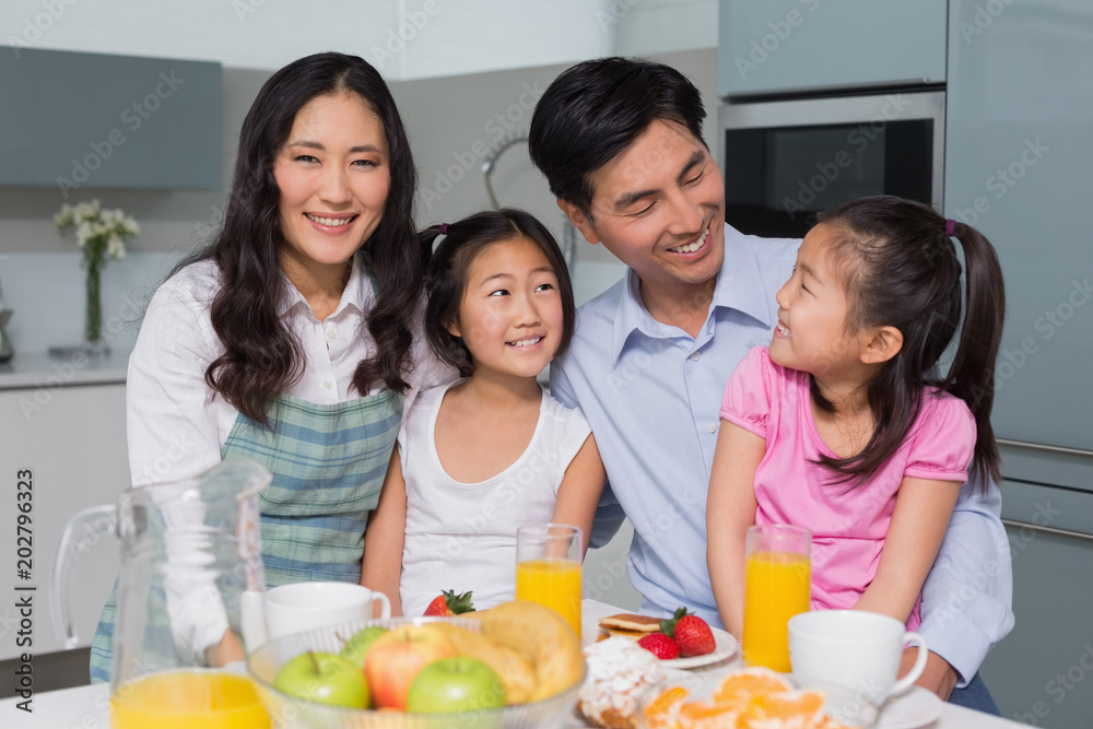 Cheerful family of four enjoying healthy breakfast in kitchen Cheerful family of four enjoying healthy breakfast in kitchen