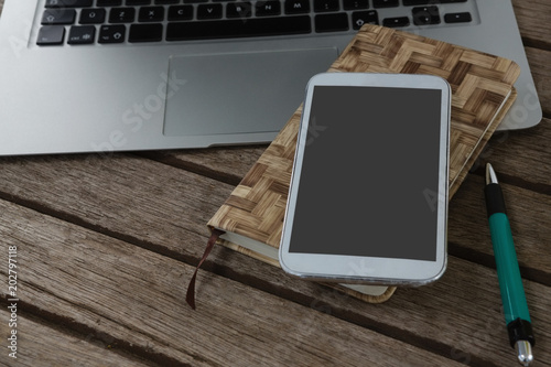 Laptop, mobile phone, dairy and pen on wooden plank