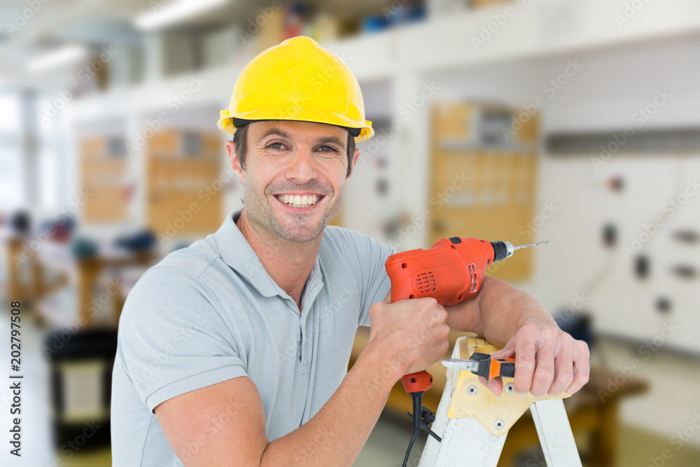 Fotografie Happy technician holding drill machine while leaning on ladder against workshop