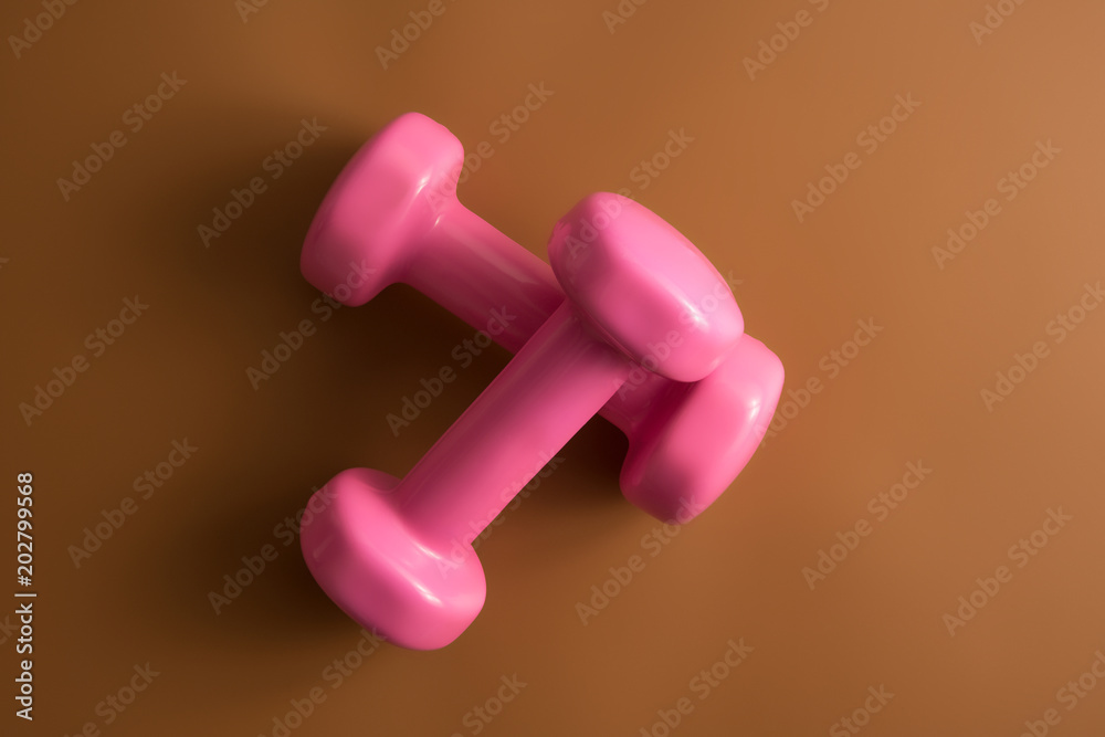 Two pink dumbbells isolated on brown color background. Top view. Flat lay Two pink dumbbells isolated on brown color background. Top view. Flat lay