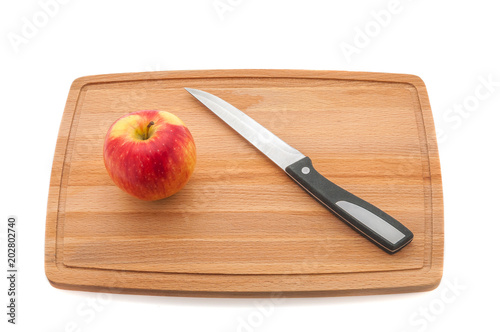 Red juicy apple and knife on a cutting board made of dark wood.