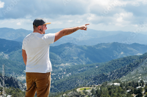 Man shows direction with his hand standing on top of cliff in summer mountains. Hiking man pointing on something with his hand, point finger. Cyprus. Copyplace, place for text photo