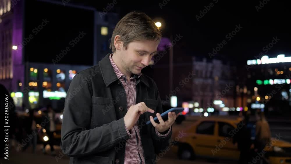 Young hipster guy using modern smartphone outdoors, man chatting with friends at social networks while walking at evening city streets, car lights close up night student Young hipster guy using modern smartphone outdoors, man chatting with friends at social networks while walking at evening city streets, car lights close up night student