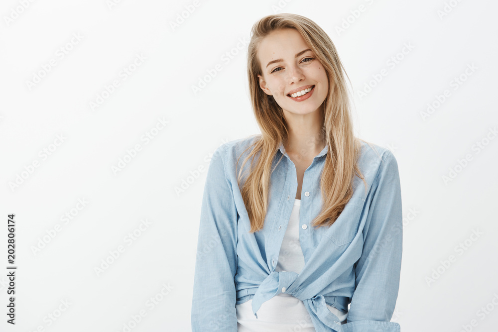 Waist-up shot of cute good-looking girlfriend with blond hair, tilting head and smiling joyfully while standing casually over gray background, being friendly and polite, ready to help with advice Waist-up shot of cute good-looking girlfriend with blond hair, tilting head and smiling joyfully while standing casually over gray background, being friendly and polite, ready to help with advice