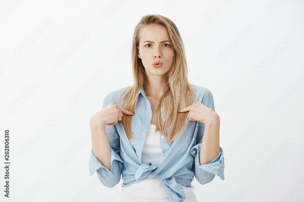 Stunned questioned european female student with blond hair, pointing at herself with clueless expression, being unexpectedly chosen, standing amazed over gray background, receiving offer Stunned questioned european female student with blond hair, pointing at herself with clueless expression, being unexpectedly chosen, standing amazed over gray background, receiving offer
