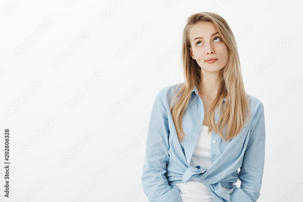 Portrait of unimpressed beautiful european woman with blond hair, smirking and looking upwards with indifferent expression, standing in stylish outfit over white background casually Portrait of unimpressed beautiful european woman with blond hair, smirking and looking upwards with indifferent expression, standing in stylish outfit over white background casually