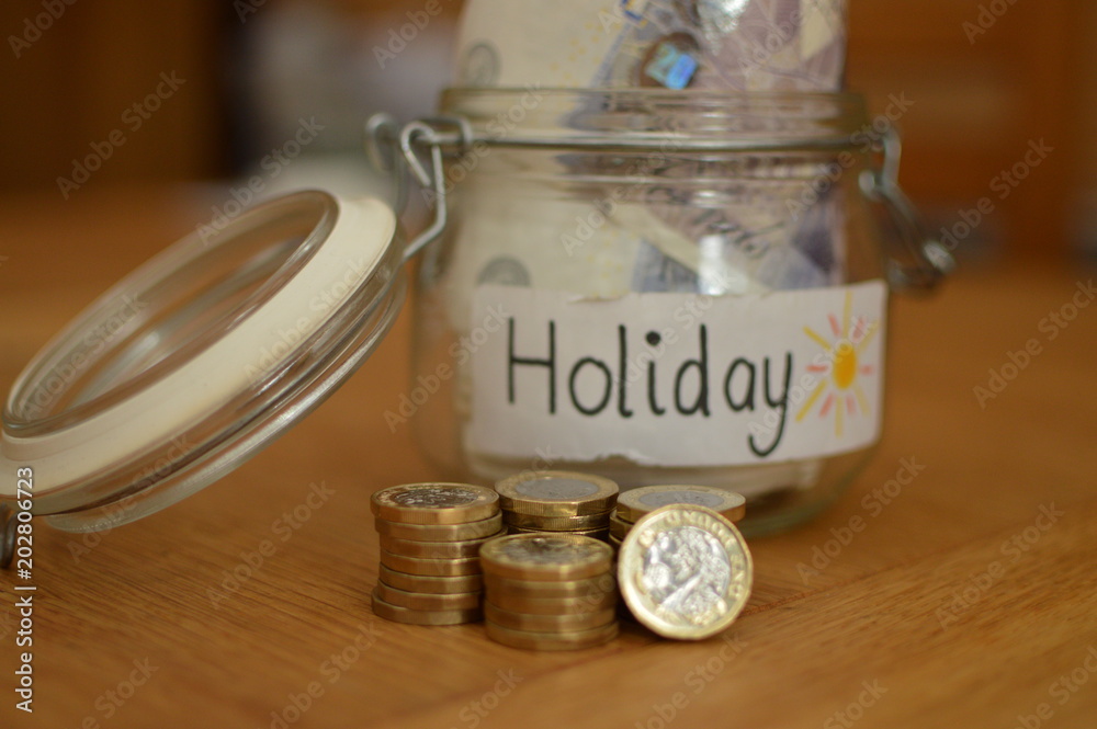 Glass holiday savings pot with currency notes and coins on wooden table Glass holiday savings pot with currency notes and coins on wooden table