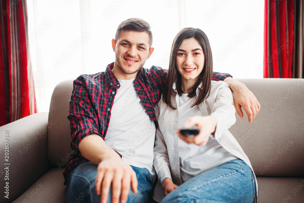 Smiling couple sitting on couch and watch tv