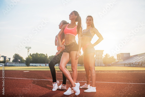 Group of fit young sportswomen standing in athletics stadium and posing.