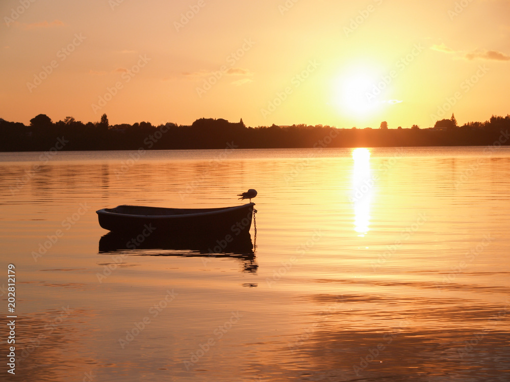 Small dinghy afloat and silhouetted on red harbour water at sunrise