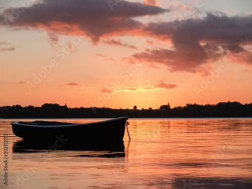 Small dinghy afloat and silhouetted on red harbour water at sunrise © Brian Scantlebury