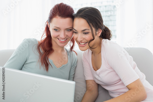 Happy young female friends using laptop at home